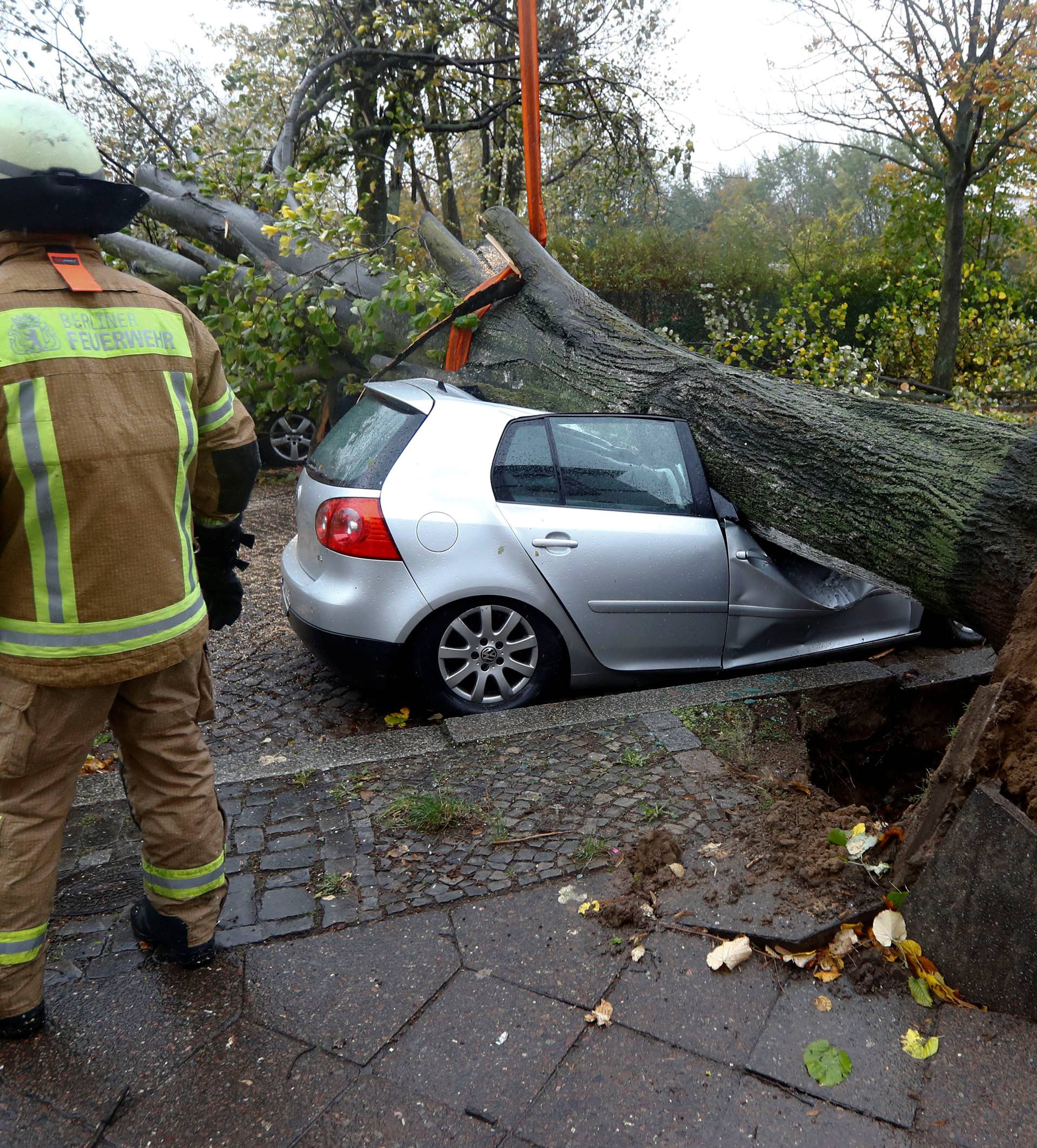 Firefighters are pictured next to a car damaged by a tree during stormy weather caused by storm called "Herwart" in Berlin
