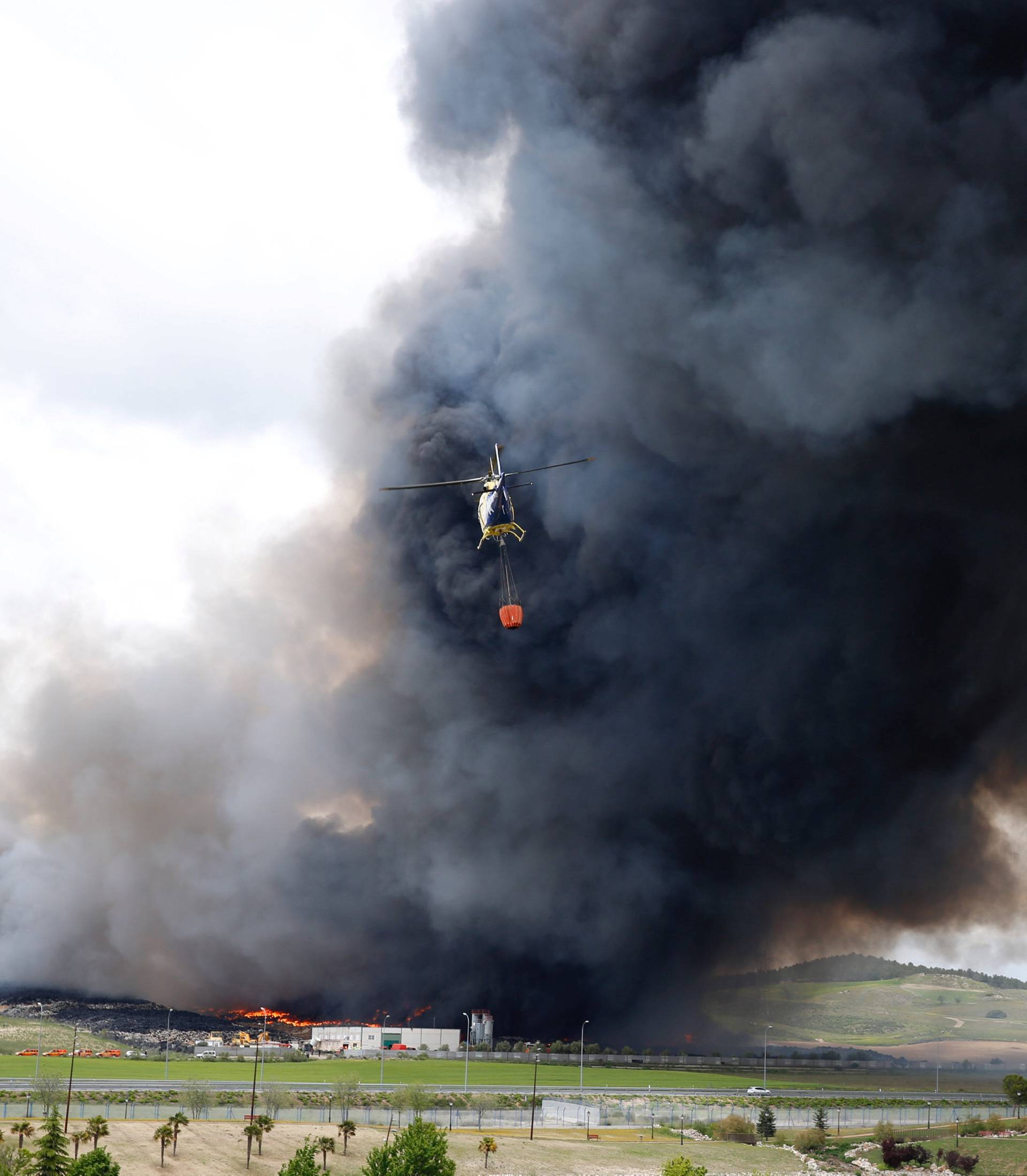 An helicopter prepares to drop water over a fire at a tyre dump near a residential development in Sesena