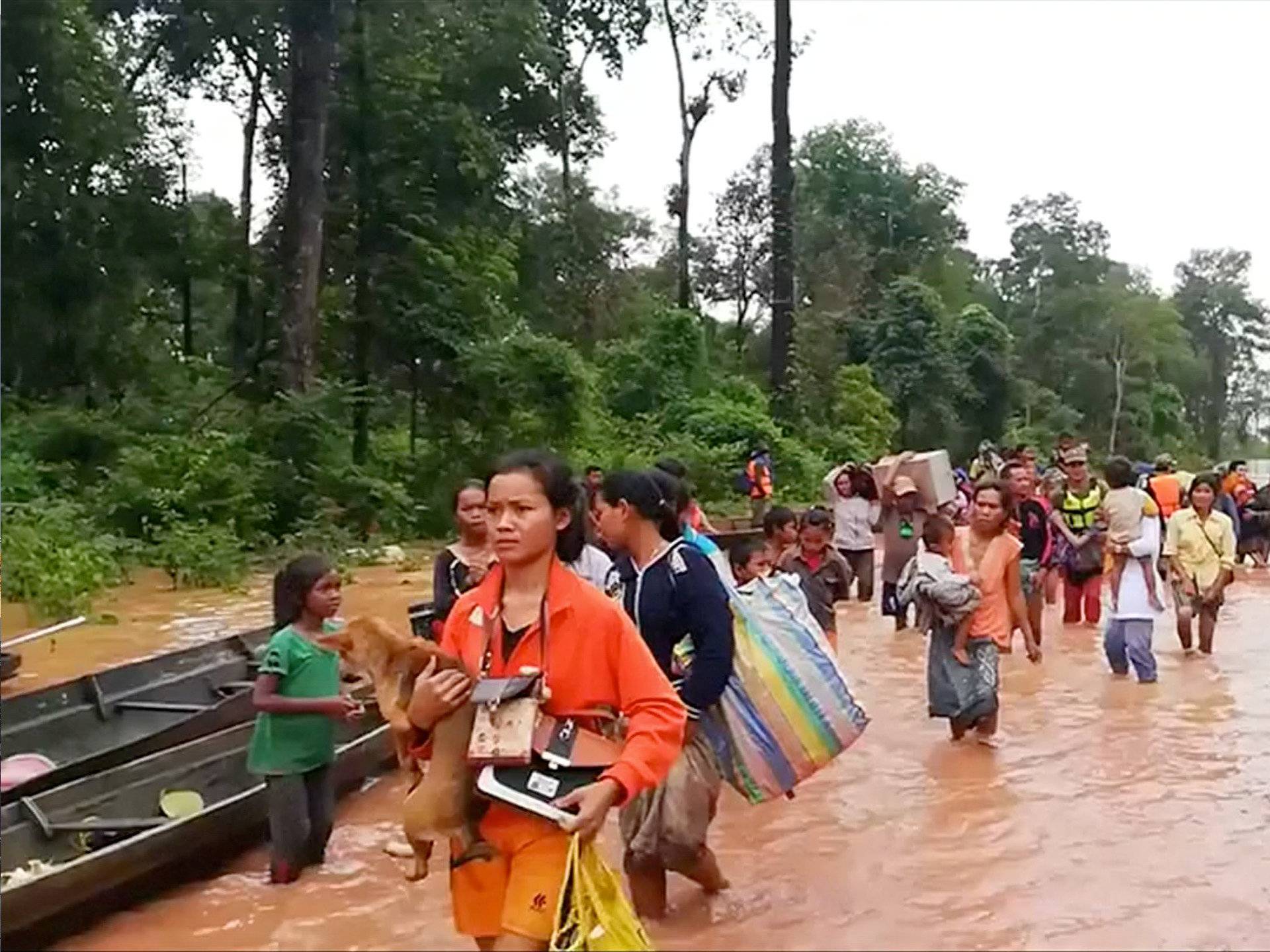 People walk through flooded area after being brought to safety by boat in Sanam Xay district, Attapeu Province, Laos after a hydropower dam under construction in Southern Laos collapsed, in this still picture taken from social media video