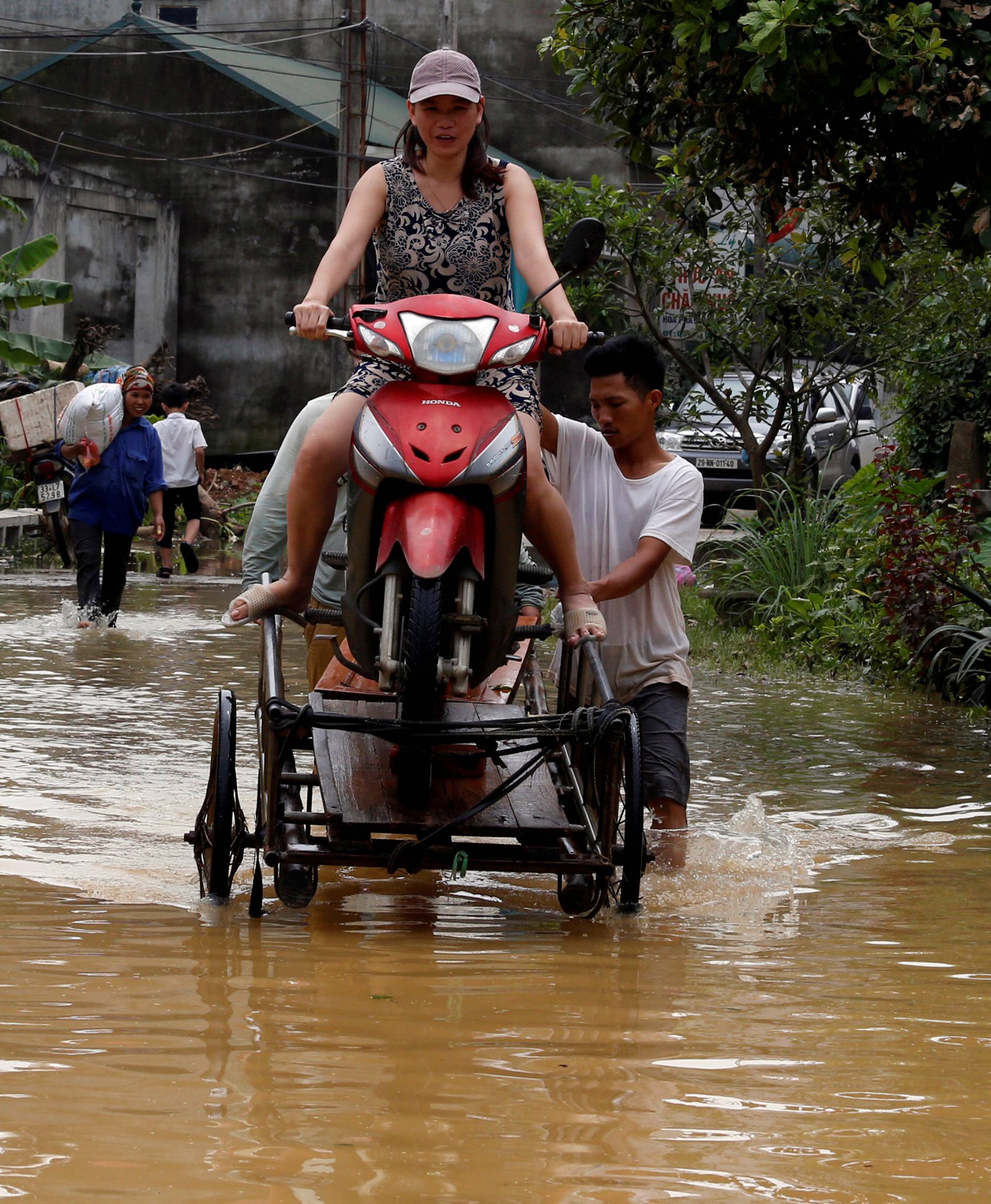 Men evacuate a woman through a flooded road after a tropical depression in Hanoi