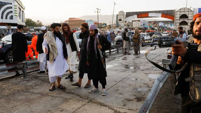Taliban fighters stand guard at the site of a blast in Kabul
