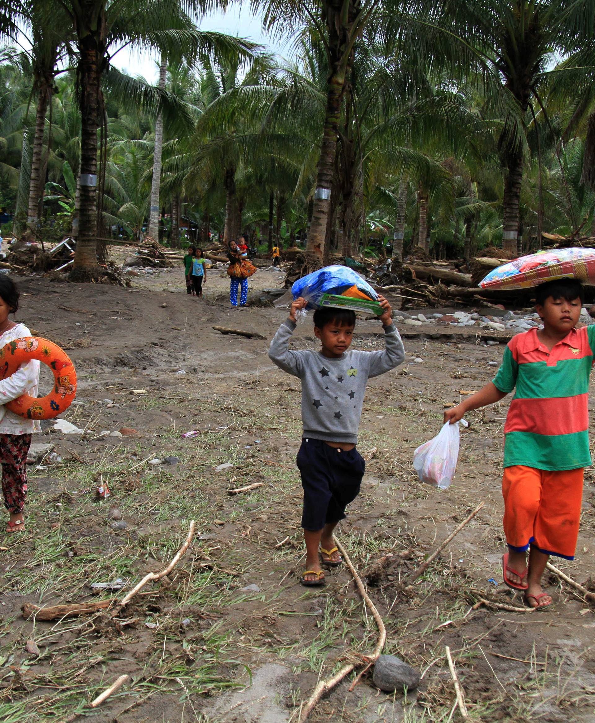 Children carry relief goods in a village devastated by flash floods in Salvador, Lanao del Norte