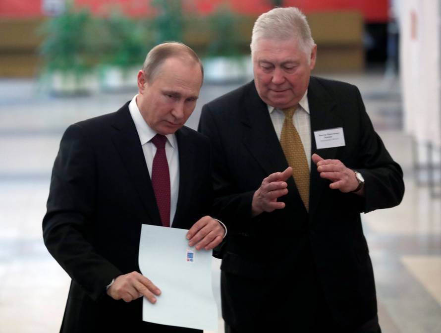 Russian President and Presidential candidate Vladimir Putin talks to a member of a local election commission at a polling station during the presidential election in Moscow