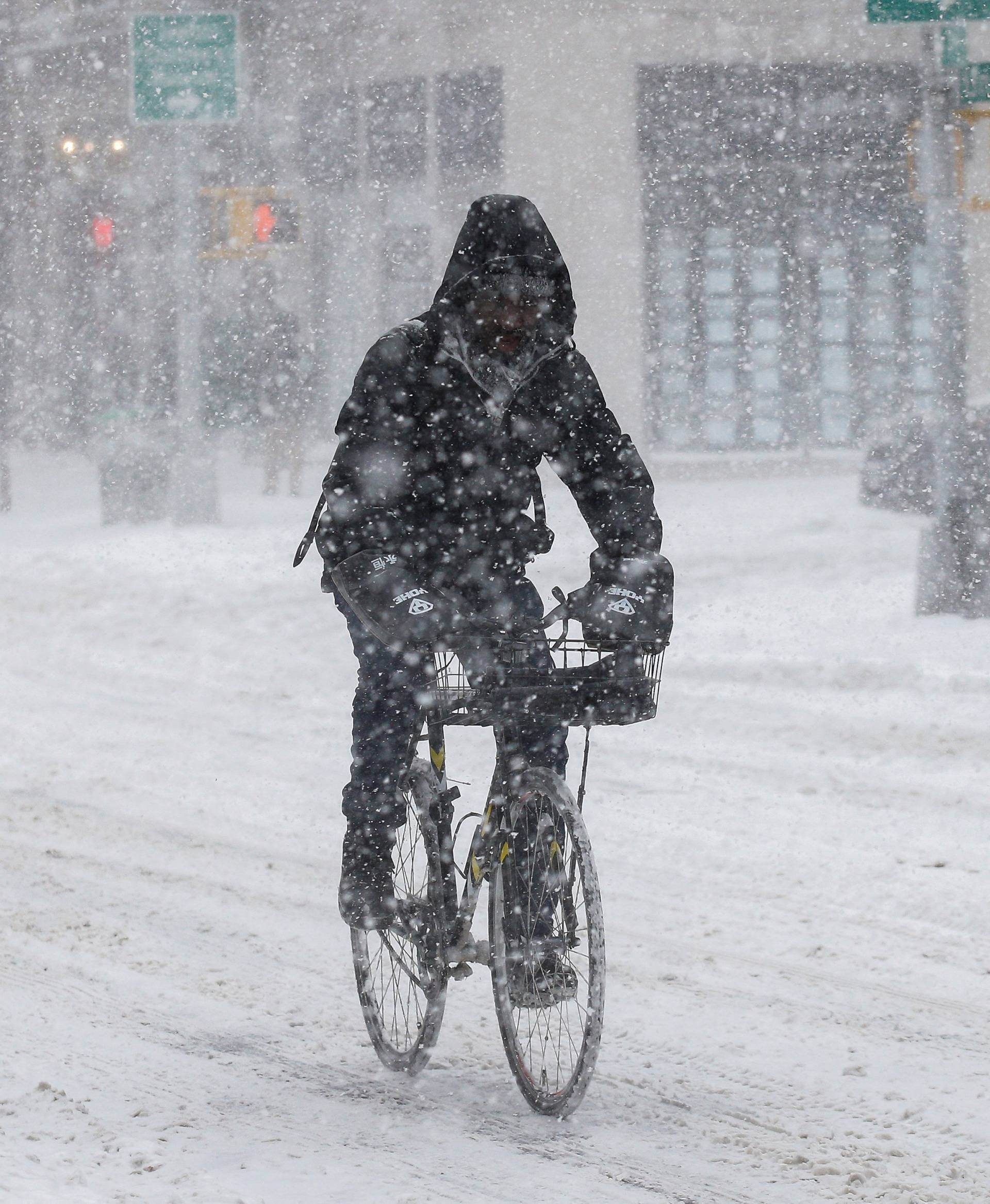 A man rides a bike in the wind and snow during a snowstorm in the Brooklyn borough of New York