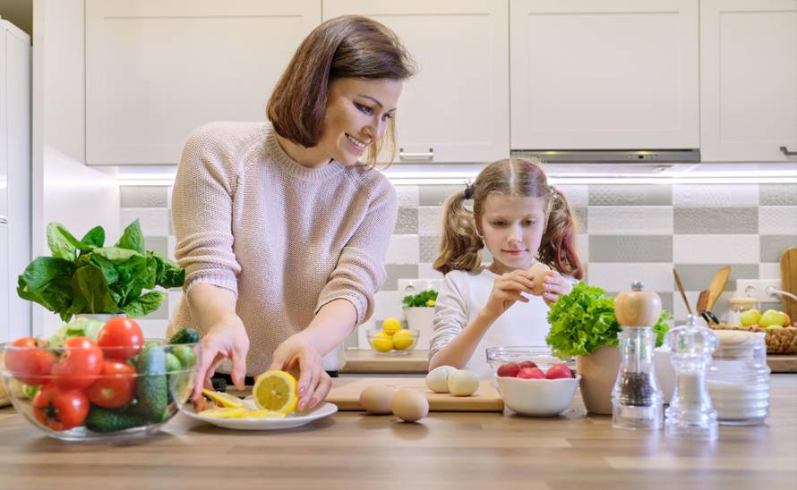 Smiling mother and daughter 8, 9 years old cooking together in kitchen vegetable salad. Healthy home food, communication parent and child.