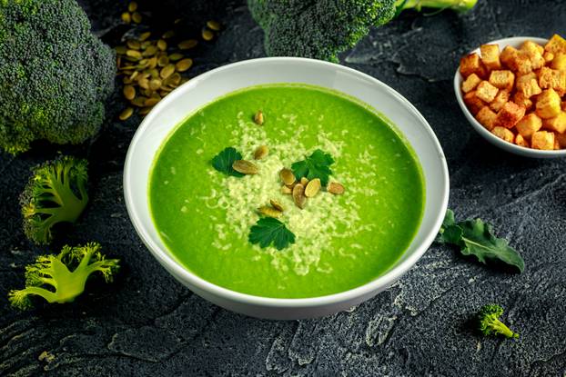 Dietary Broccoli smooth cream soup with sprinkle of sunflower seeds, parsley leaves and croutons on stone table.