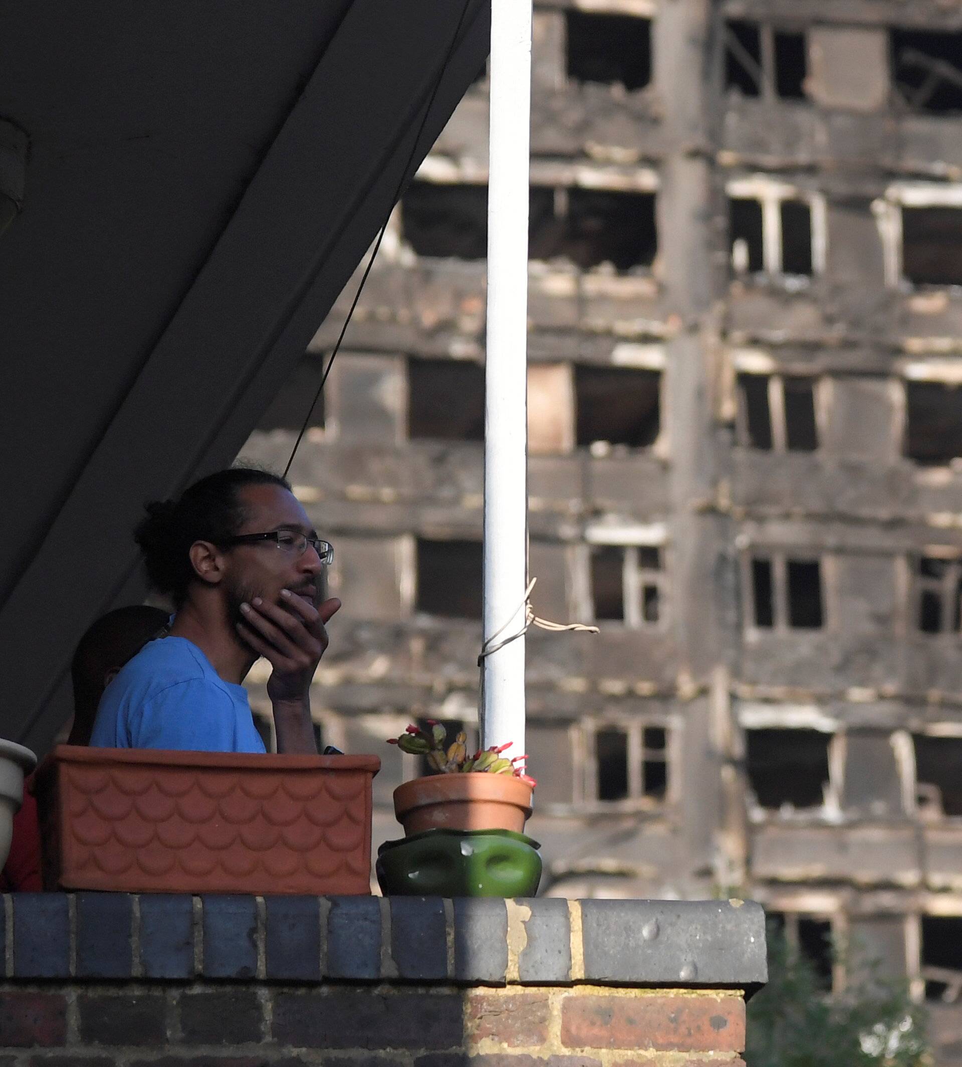 A man looks out from a balcony in front of the Grenfell Tower block that was destroyed in a fire, in north Kensington, West London