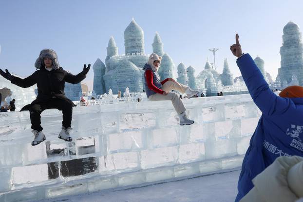 Visitors pose on an ice wall at the annual Ice and Snow Festival in Harbin