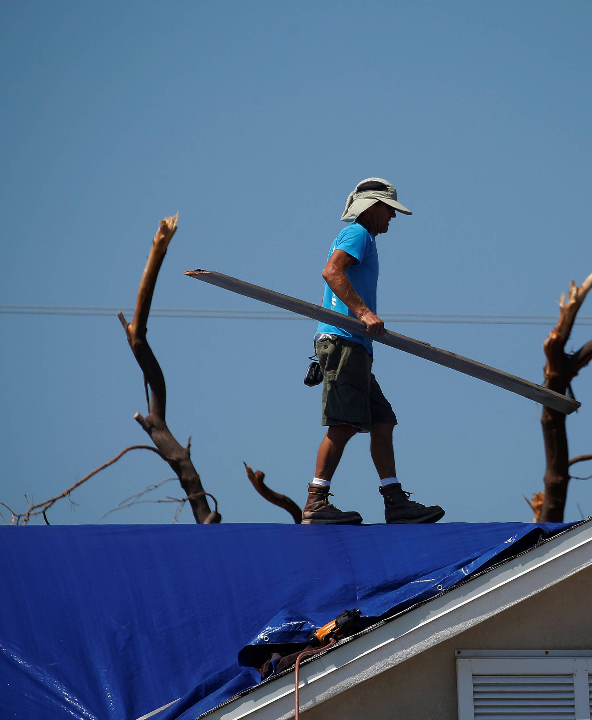 A roofer works on attaching a blue tarp to a roof following Hurricane Irma in Ramrod Key, Florida