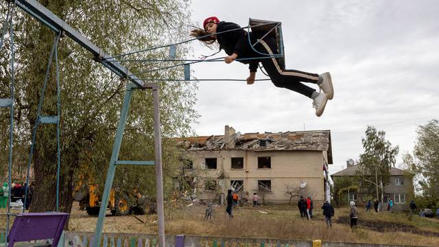 A child sits on a swing near an apartment building that was damaged by the impact of a Russian S-300 missile in Peresichne near Kharkiv