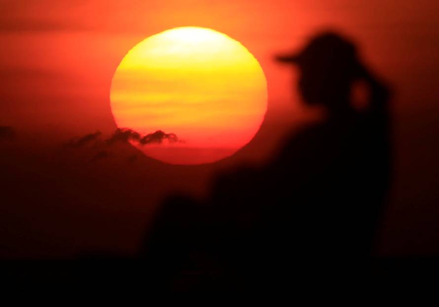 A woman is silhouetted as she watches the sun set along the coast of Manila bay in Metro Manila
