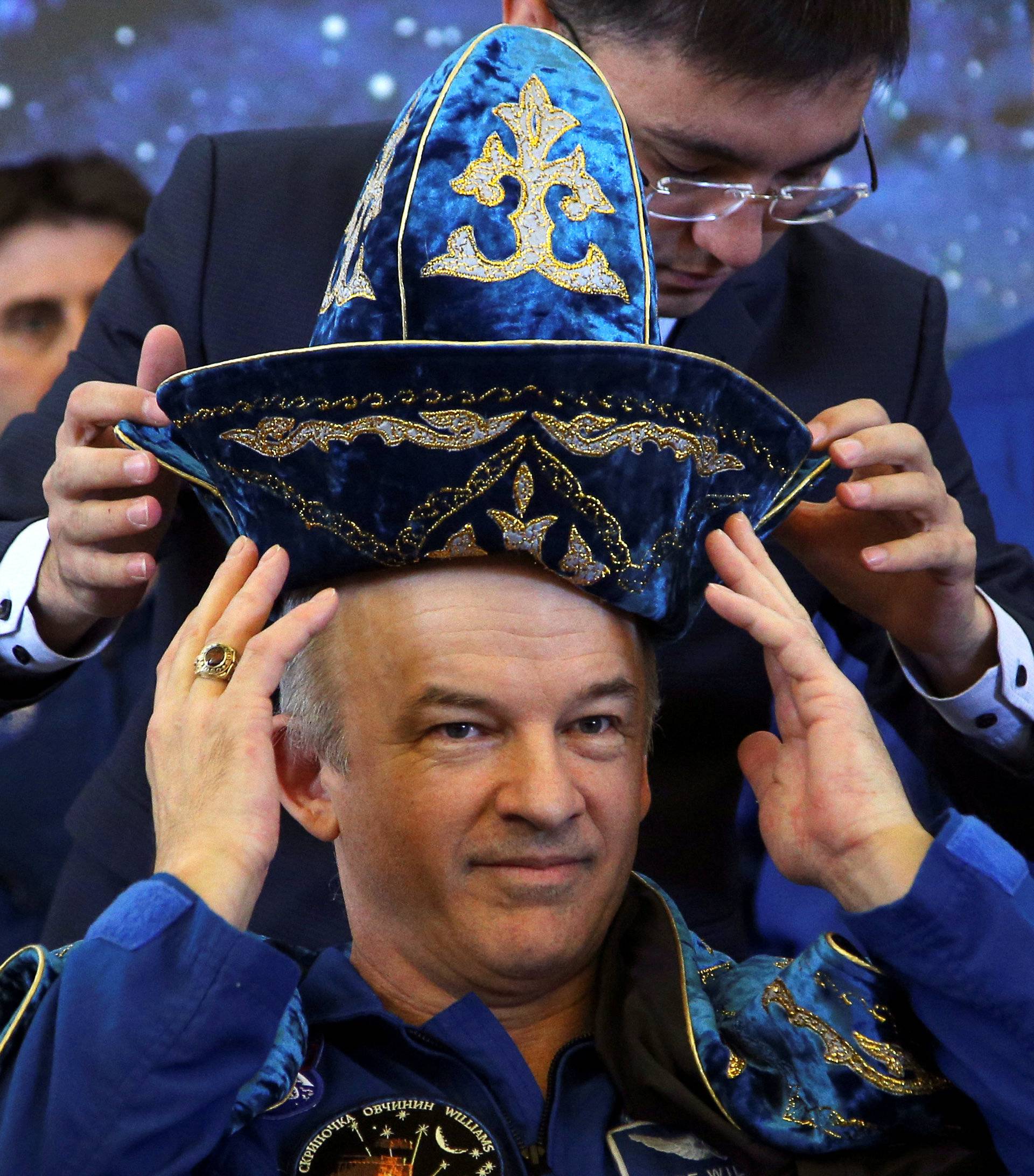 The International Space Station (ISS) crew member Jeff Williams of the U.S. adjusts Kazakh national costume presented to them at a news conference in Karaganda, Kazakhstan