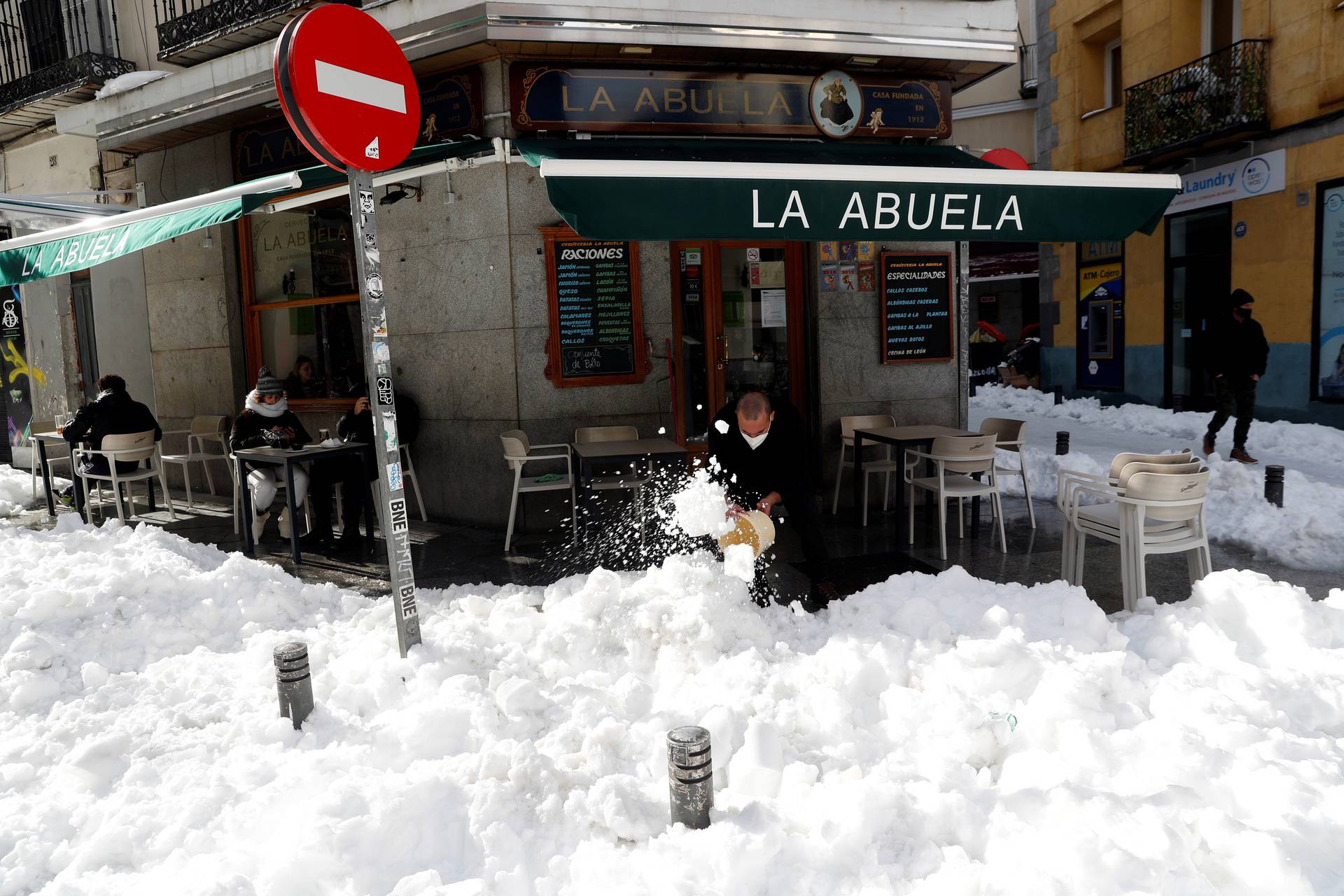 An employee of a restaurant clears snow as customers sit at an outdoor terrace in Madrid
