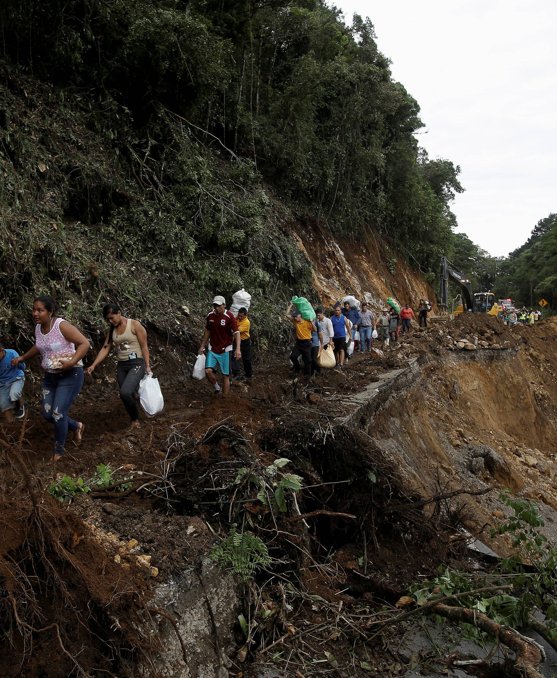 People traveling by bus for two days and were trapped between landslides walks in an area of a highway collapsed by Storm Nate in Casa Mata, Costa Rica