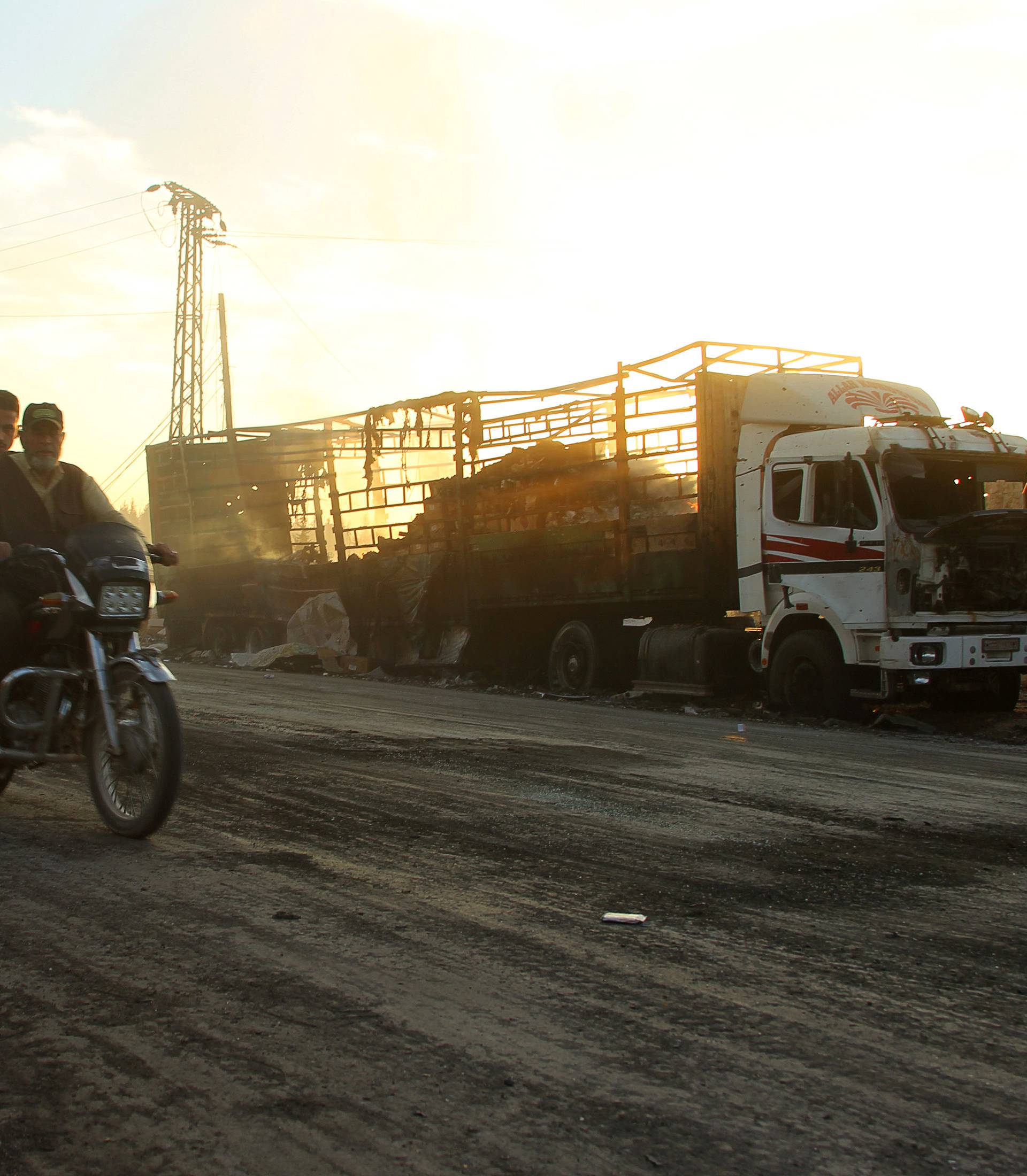 Men drive a motorcycle near a damaged aid truck after an airstrike on the rebel held Urm al-Kubra town