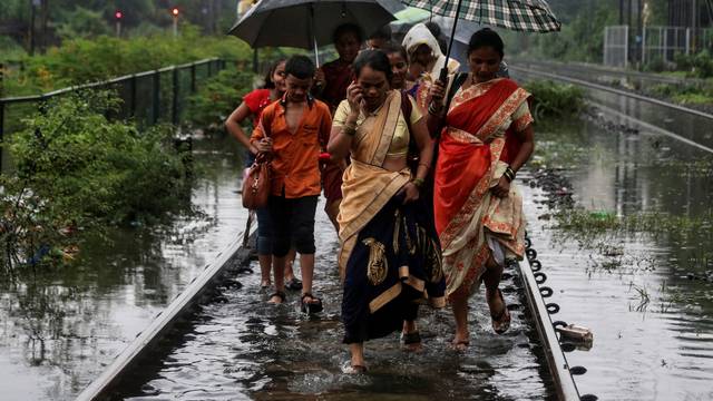 Commuters walk on waterlogged railway tracks after getting off a stalled train during heavy monsoon rains in Mumbai