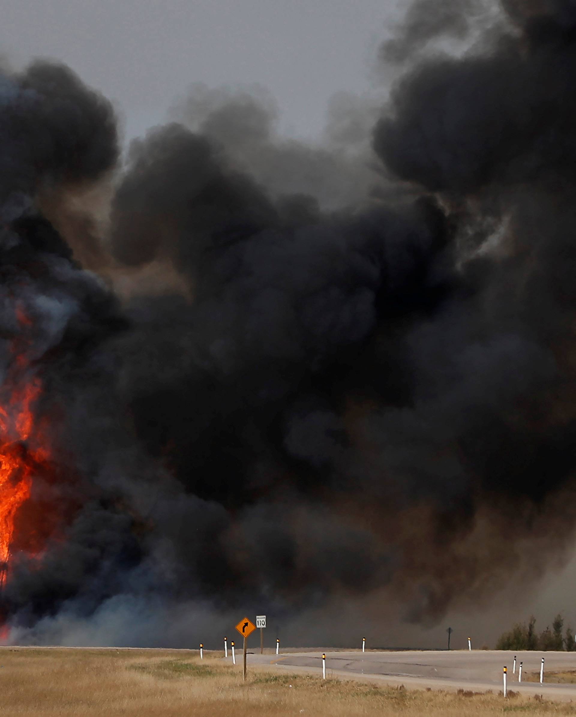 Smoke and flames from the wildfires erupt behind a car on the highway near Fort McMurray