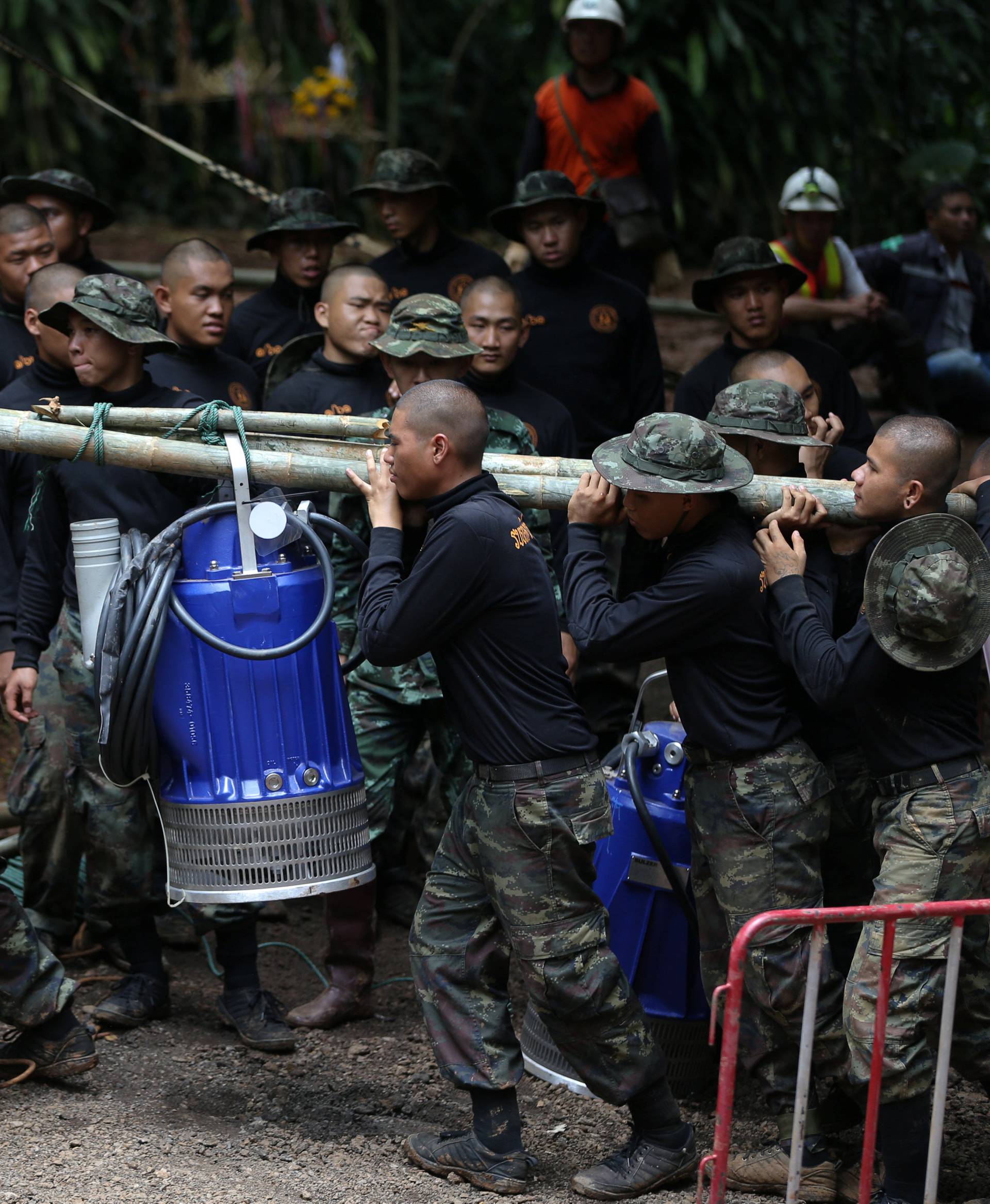 Military personnel carry a water pump machine as they enter the Tham Luang cave complex, where 12 boys and their soccer coach are trapped, in the northern province of Chiang Rai