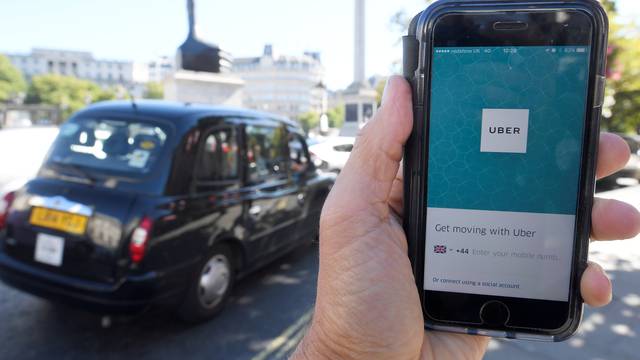 A photo illustration a London taxi passing as the Uber app logo is displayed on a mobile telephone, as it is held up for a posed photograph in central London