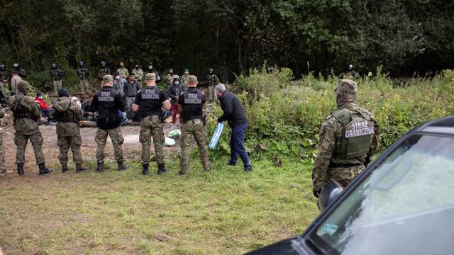 Polish border guard officers stand guard next to a group of migrants stranded on the border between Belarus and Poland near the village of Usnarz Gorny