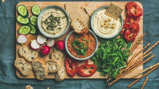 Flat-lay of Vegetarian dips hummus, babaganush, muhammara on wooden board