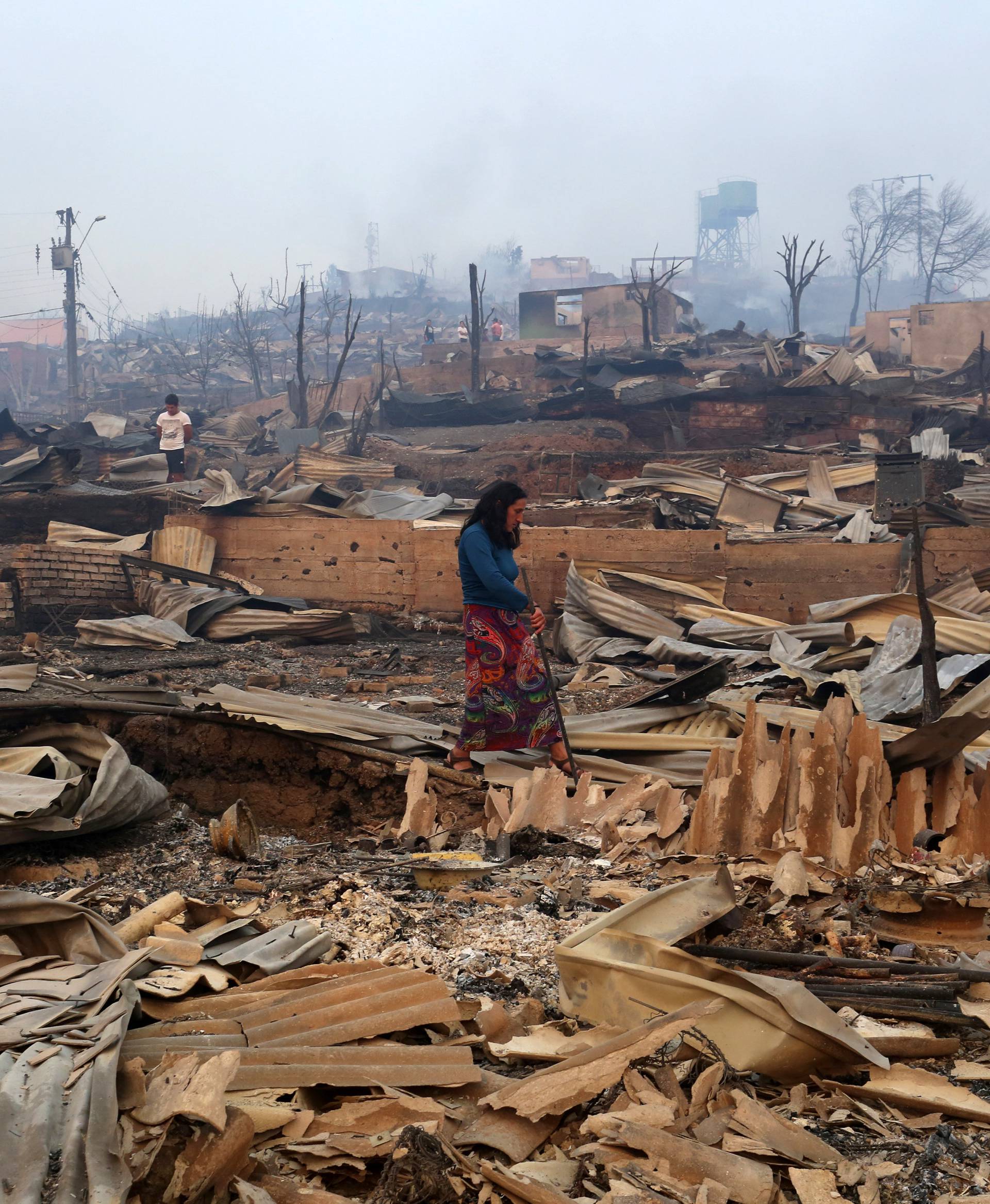 A woman walks through the remains of burnt houses as the worst wildfires in Chile's modern history ravage wide swaths of the country's central-south regions, in Santa Olga