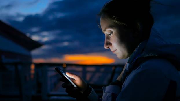 Woman using vertical smartphone on deck of cruise ship at night