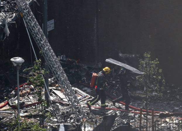 A police officer holds a riot shield over a firefighter at a tower block severely damaged by a serious fire, in north Kensington, West London