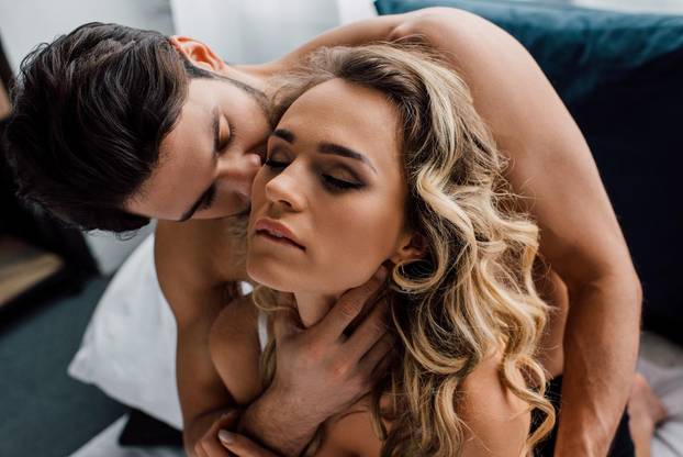 Handsome man kissing and touching neck of sexy girlfriend on bed