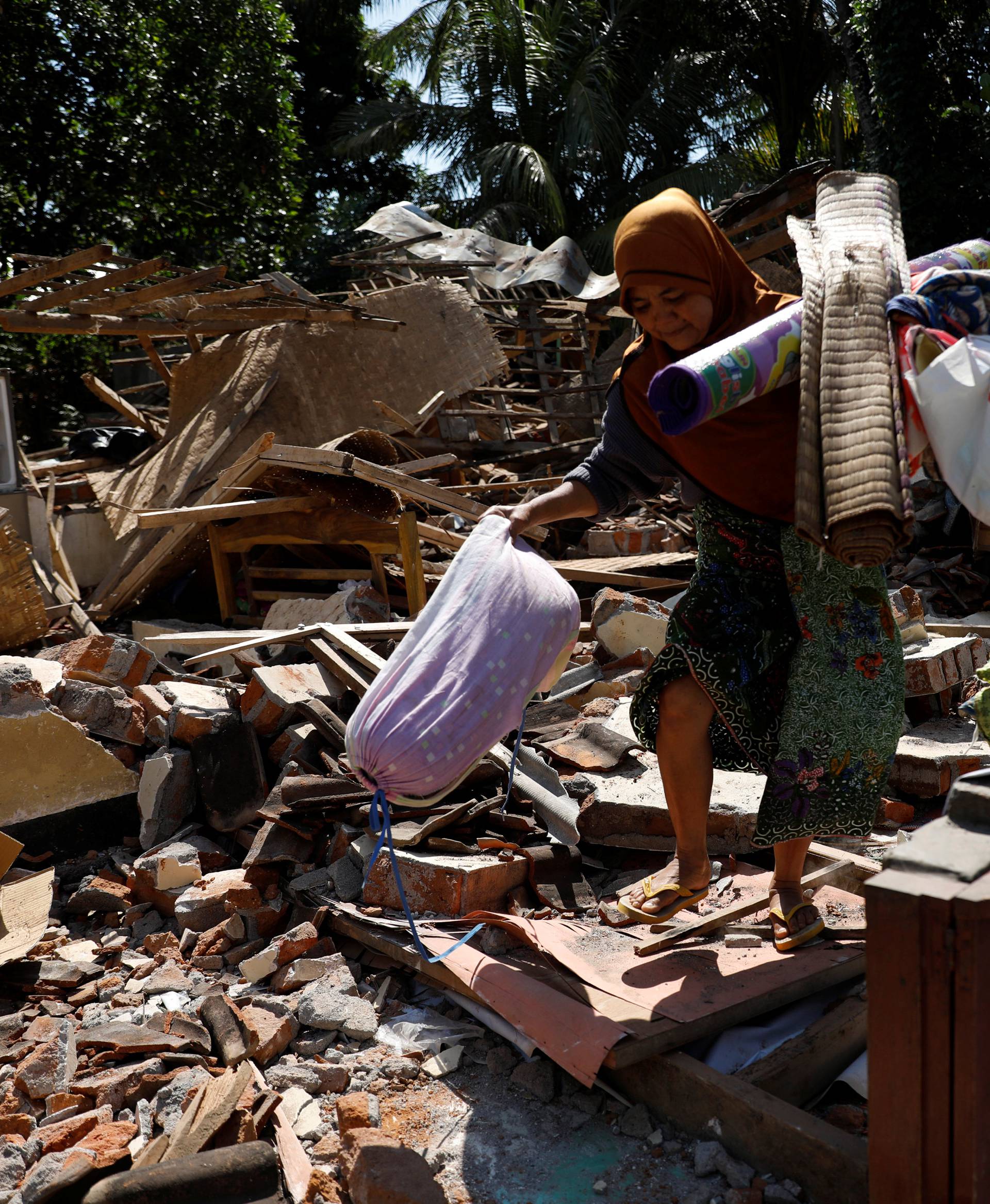 A woman carries valuable goods from the ruins of her house at Kayangan district after earthquake hit on Sunday in North Lombok