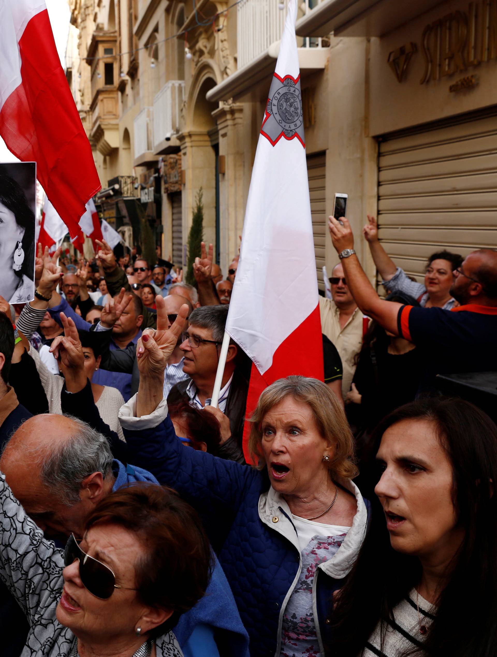 A demonstrator carries a photo of assassinated anti-corruption journalist Daphne Caruana Galizia as others sing the national anthem at the end of a protest against government corruption revealed by the Daphne Project, in Valletta