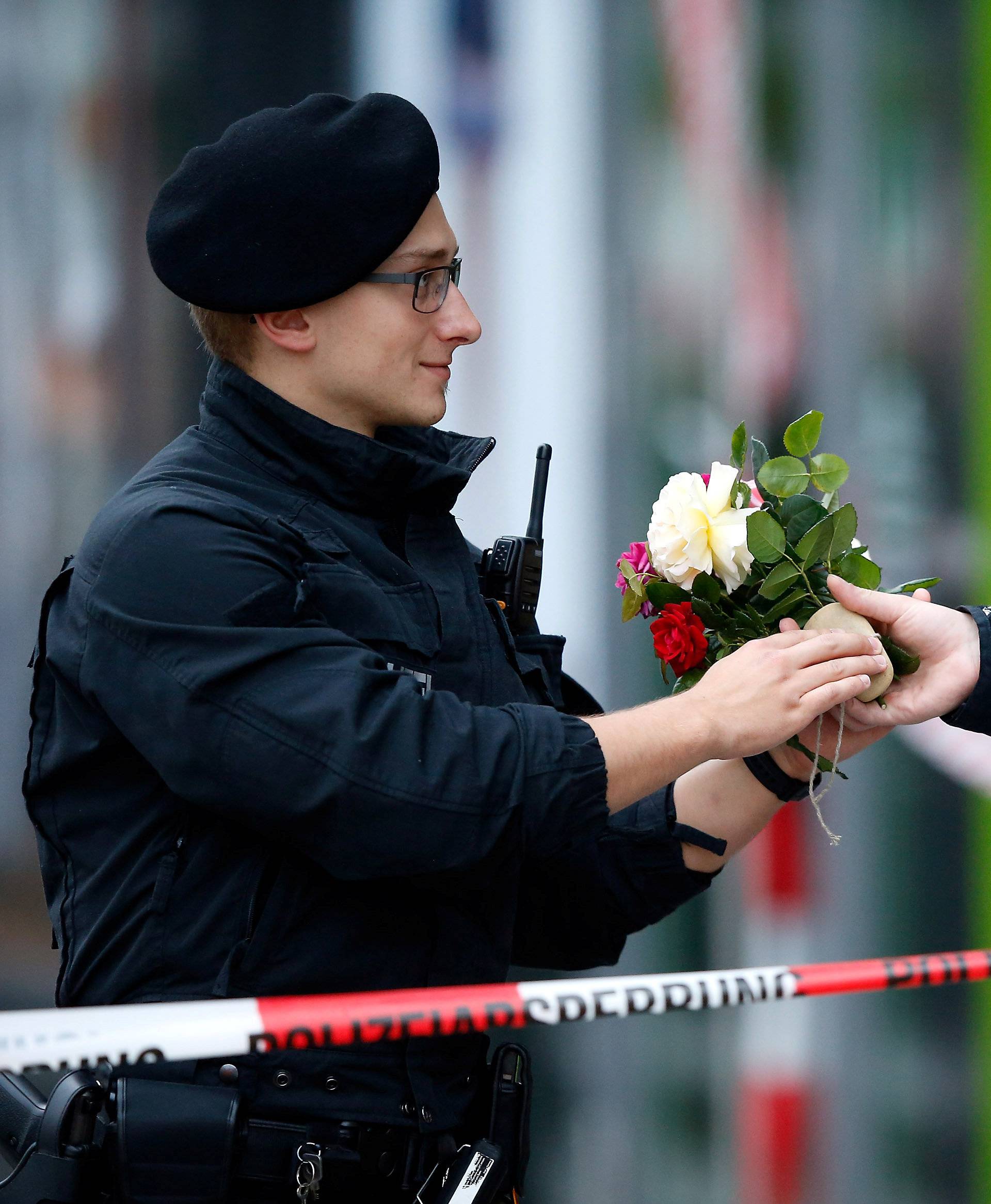 A pedestrian hands flowers to a policeman to place it near the Olympia shopping mall, where yesterday's shooting rampage started, in Munich