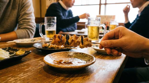 Hand Holding Yakitori Skewer At Dining Table