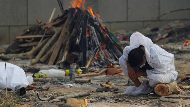 A man mourns as he sits next to the burning pyre of a relative, who died from the coronavirus disease (COVID-19), at a crematorium in New Delhi,
