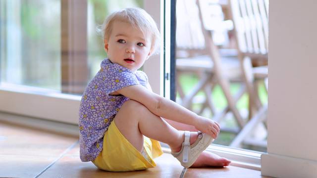Toddler girl putting shoes sitting on floor next to window