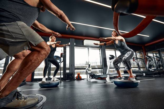 The guy tries to keep his balance on the balancing platform. Massive outdoor exercise with the help of a fitness trainer.