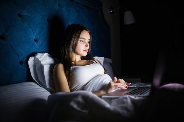 Sexy Attractive Young Woman Relaxing in Bed With Laptop Computer. Woman working on laptop in the night in bed. Woman chating in laptop in the night