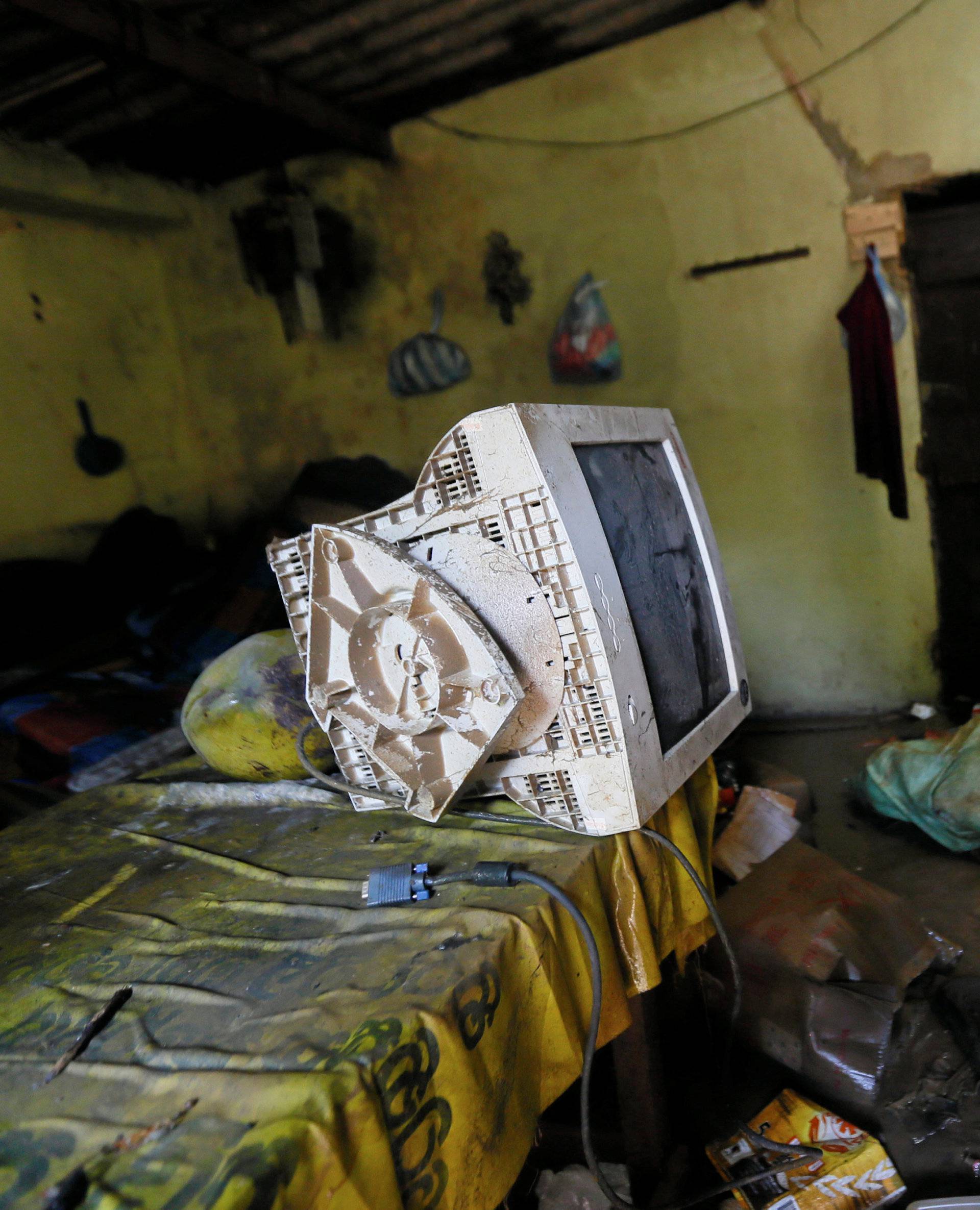 A man stands near a damaged computer monitor inside a house which was affected by the floods in Biyagama