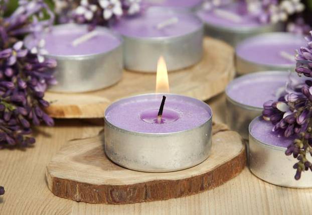 Scented candles on a wooden stand with lilac flowers on the tabl