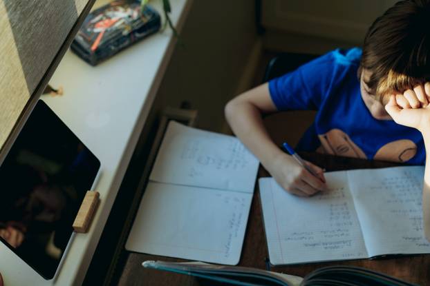 stressed tired boy doing homework at home at the desk by the window.