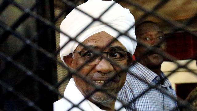FILE PHOTO: Sudanese former president Omar Hassan al-Bashir smiles inside a cage as he faces corruption charges in a court in Khartoum