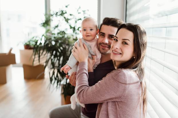 A Portrait of Young Couple with a Baby and Cardboard Boxes Moving in a New Home.