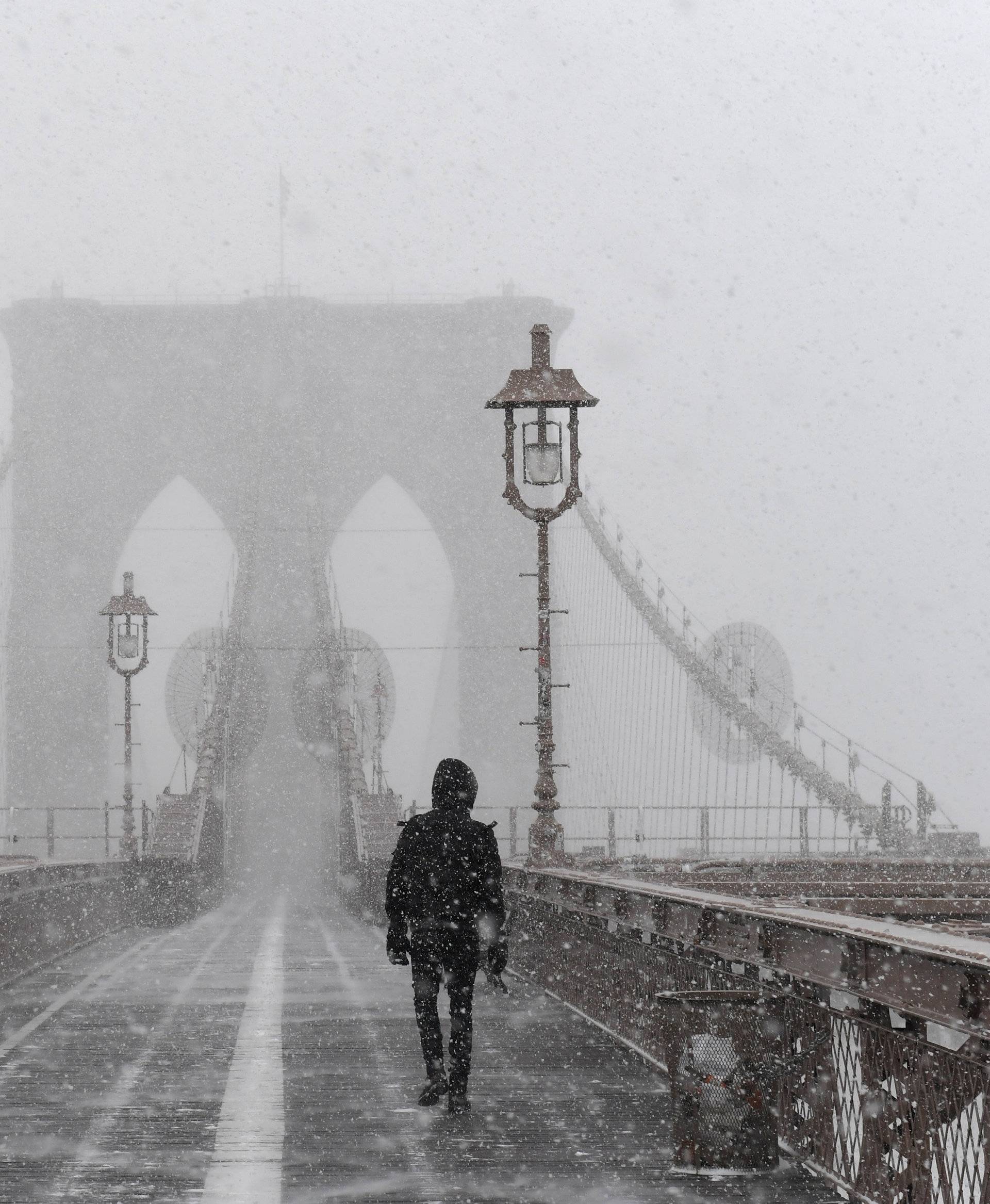 A pedestrian walks through blinding snow across the Brooklyn Bridge during Storm Grayson in New York City