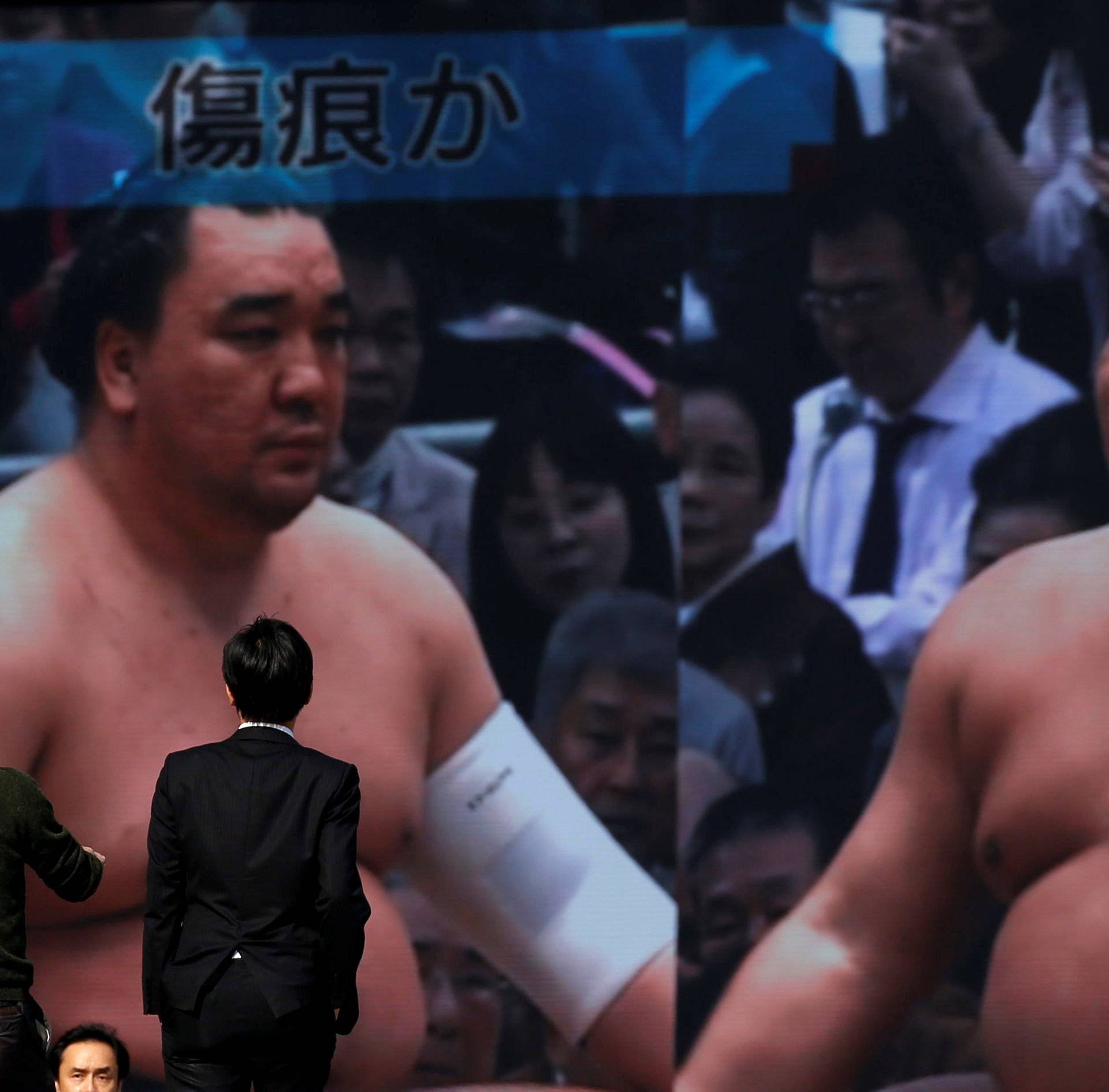People walk past a street monitor showing Sumo grand champion Harumafuji and junior wrestler Takanoiwa in Tokyo