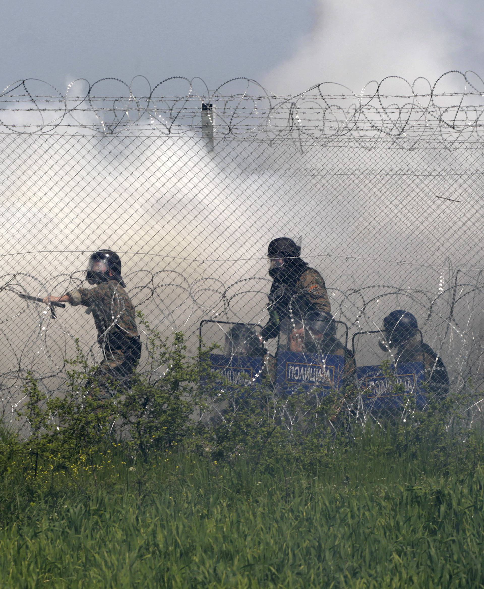 Macedonian police officers stand amid teargas smoke during clashes with protesting migrants from the Greek side of of the Greek-Macedonian border near the village of Idomeni