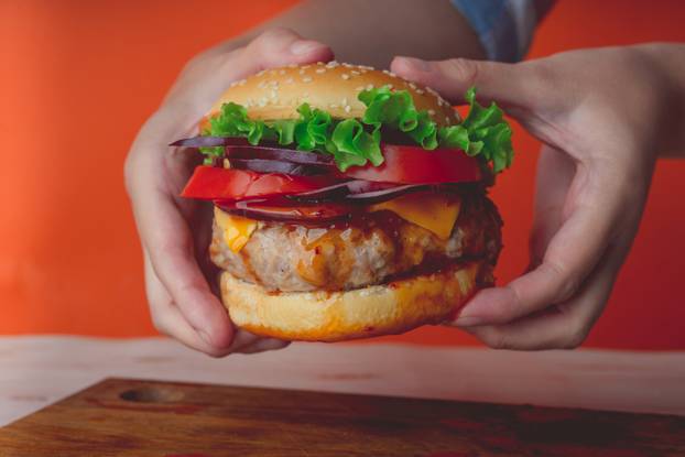 Women's hands are holding a huge juicy hamburger on orange background. Cheeseburger of the homemade.