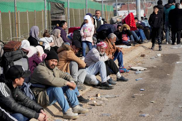 People sit as they wait to cross into Lebanon at the Masnaa border crossing between the Lebanon and Syria