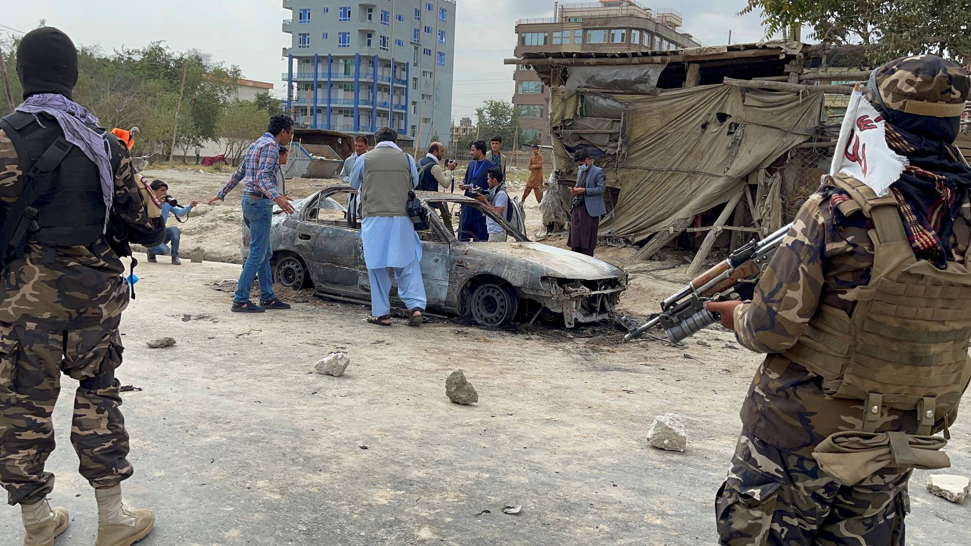 Afghan men take pictures of a vehicle from which rockets were fired, as Taliban forces stand guard, in Kabul