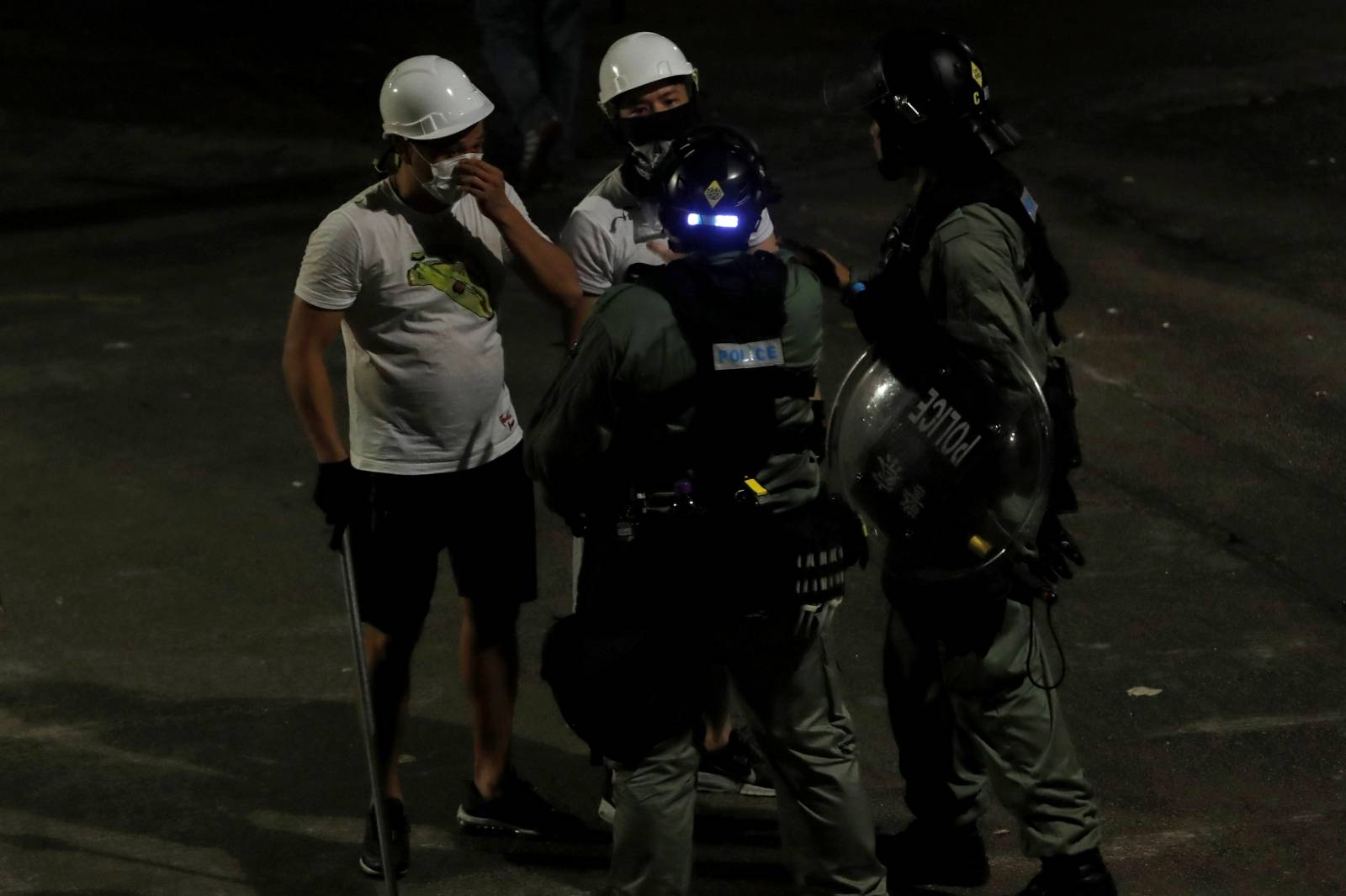 Men in white T-shirts and carrying poles talk to riot police in Yuen Long after attacking anti-extradition bill demonstrators at a train station in Hong Kong