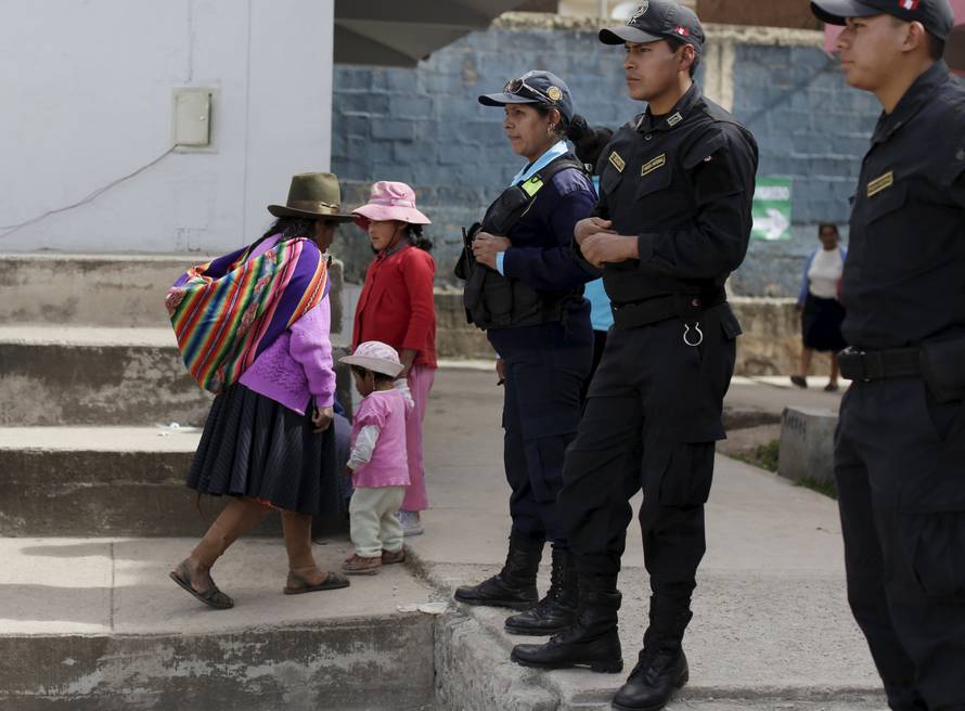 A woman walks near police officers during presidential election at a polling station in Cuzco